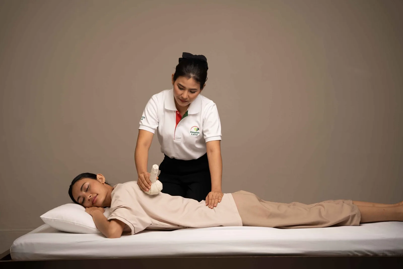 Health Land therapist applying a steamed herbal compress to a clothed client's back